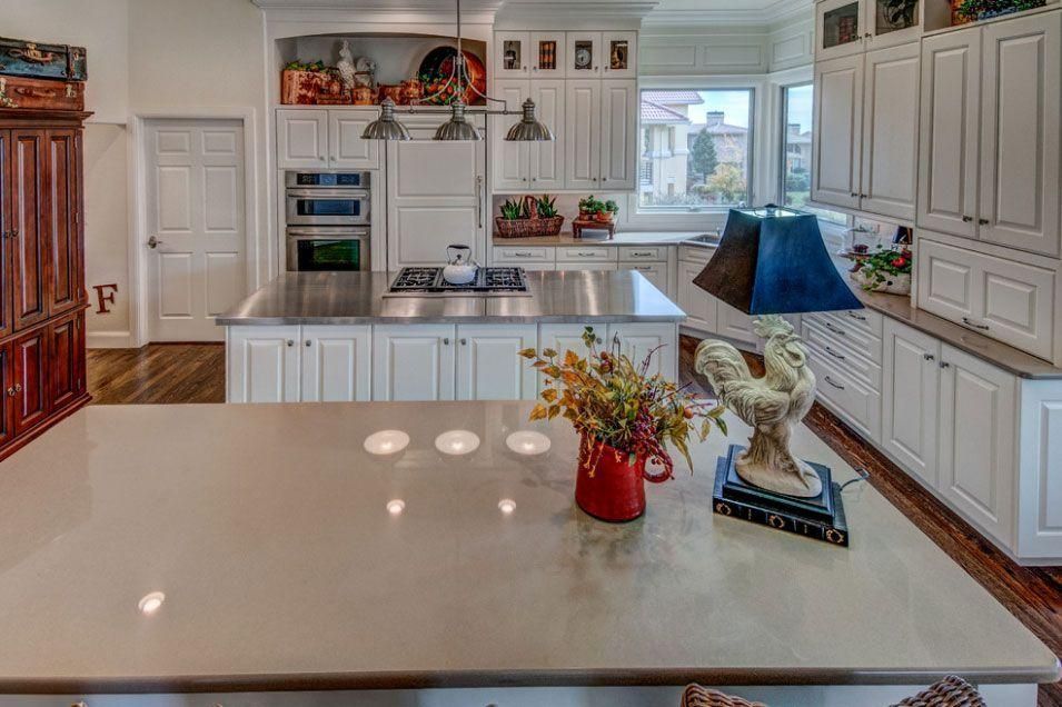 Bright white kitchen with marble island, wood floors, built-in cabinets, and a window over the sink.