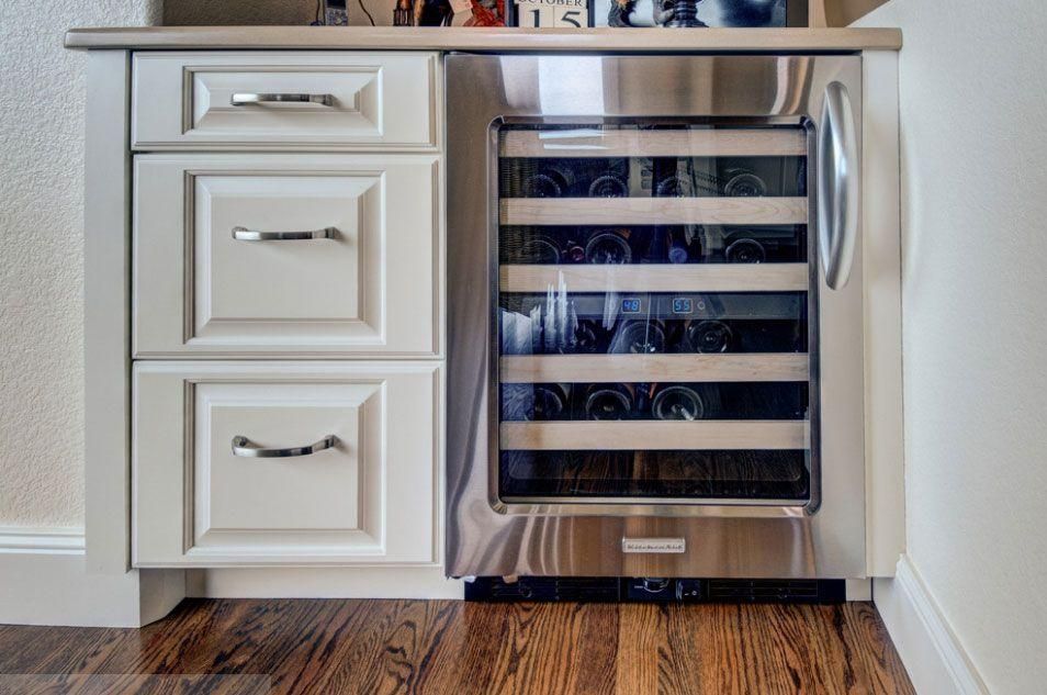 Kitchen cabinet with built-in stainless steel wine cooler and white drawers underneath.