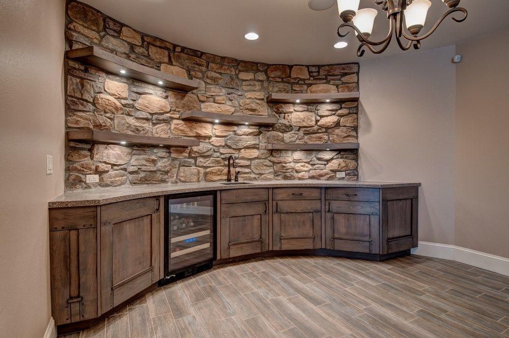 Curved wet bar with wood cabinets, stone accent wall, and chandelier in a finished basement
