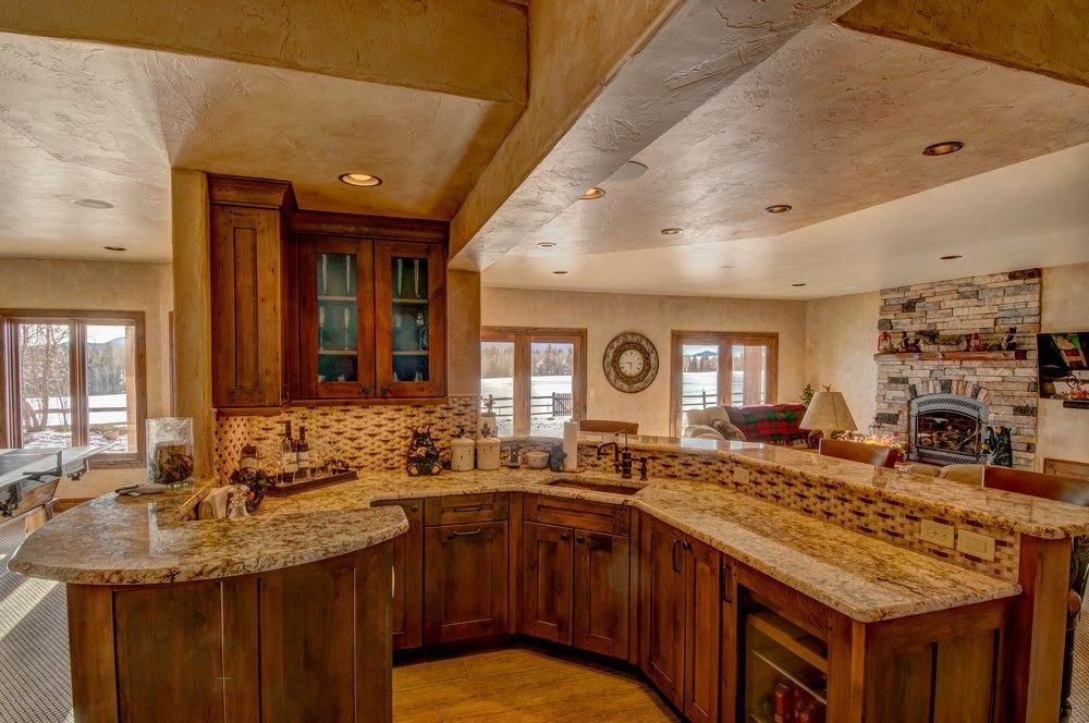 Spacious kitchen with granite island, wood cabinets, and stone fireplace in the background
