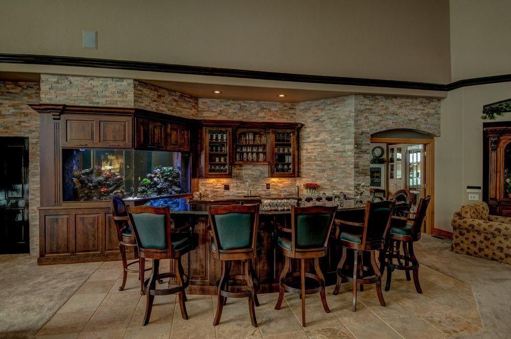 Stylish home bar with dark wood cabinets, stone wall, and bar stools in a warmly lit open room