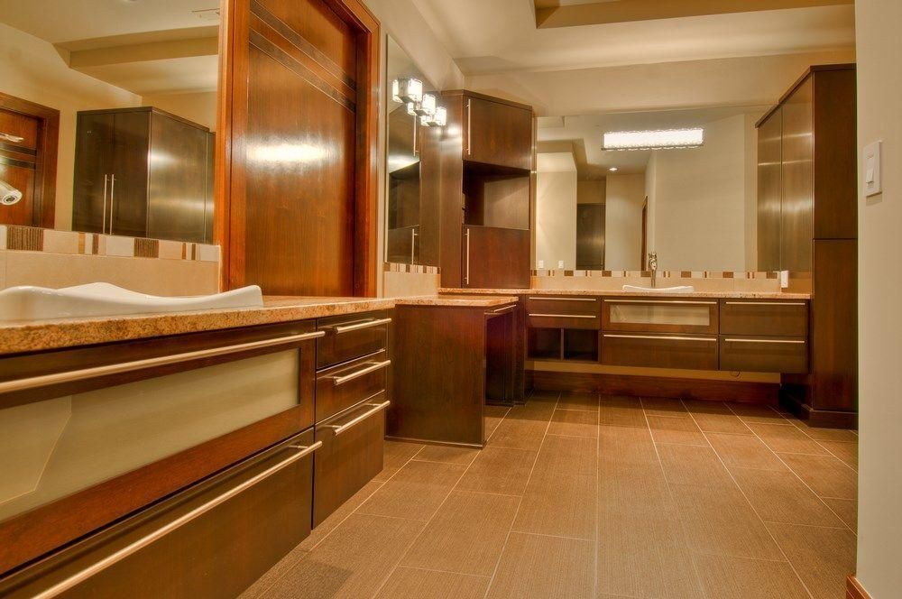 Modern bathroom with wood cabinetry, large mirrors, beige tile floor, and vanity lighting
