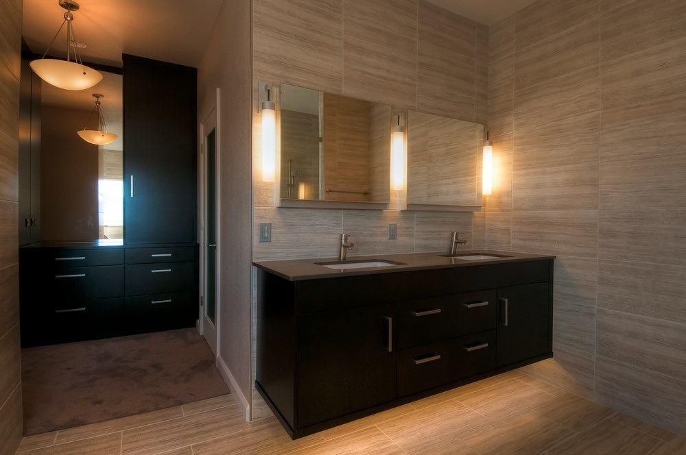 Modern bathroom vanity with black cabinets, twin sinks, and wall sconces in a tiled beige room