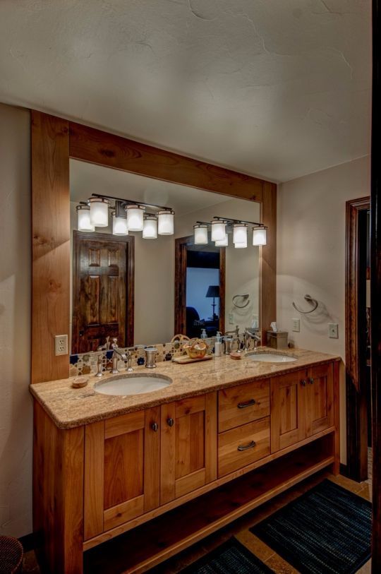 Wooden bathroom vanity with double sinks, large mirror, and light fixtures above a dark rug