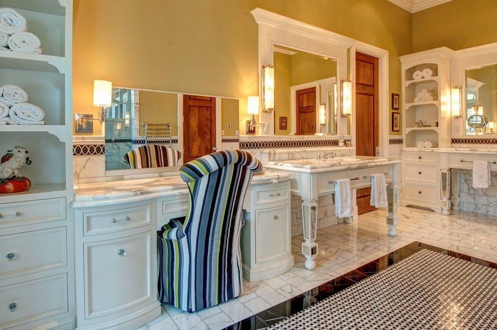 Bright bathroom vanity with double sinks, large mirror, white cabinets, and striped towel in a warm-lit room