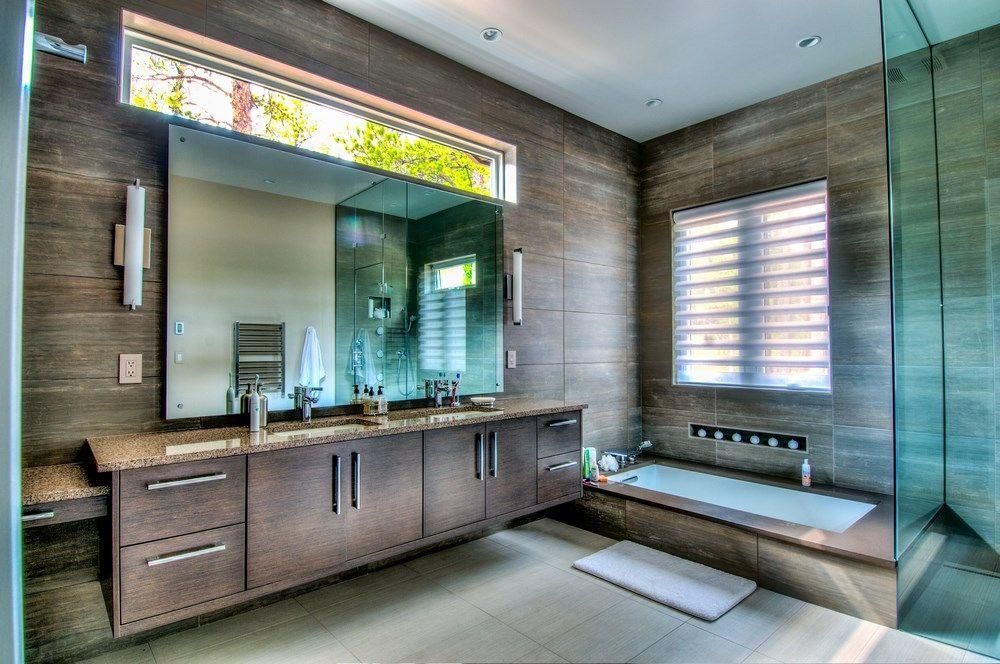 Modern bathroom with double vanity, large mirror, glass shower, and window bench.