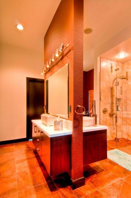 Modern bathroom with double sink vanity, large mirror, and glass shower in warm orange tones