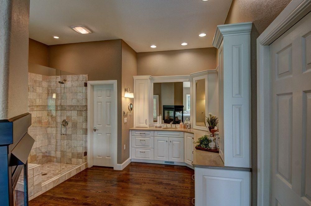 Spacious bathroom with tiled shower, white vanity, and wood floor under recessed lighting