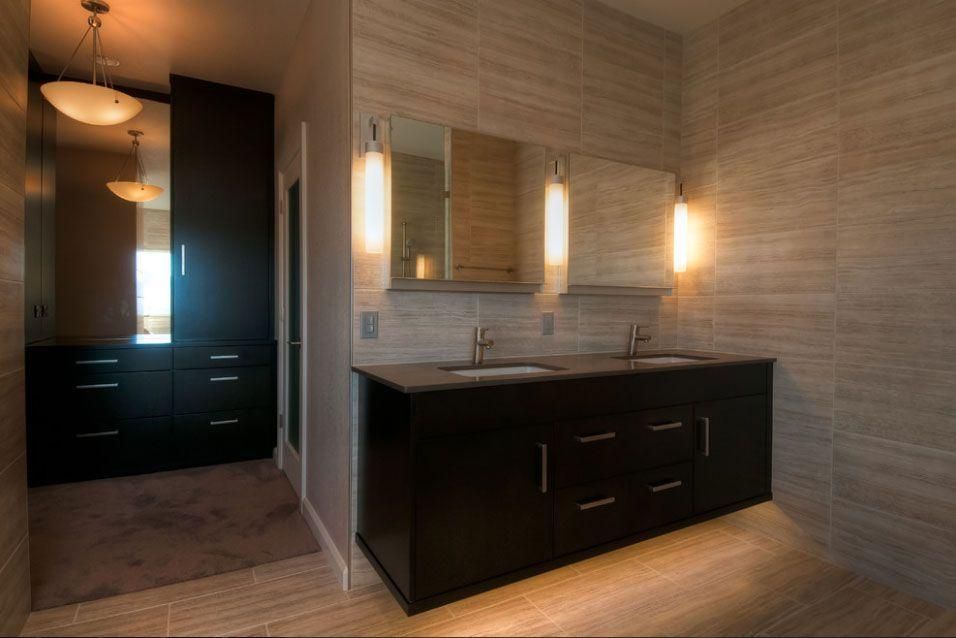 Modern bathroom with dark vanity, lit wall mirrors, and tiled walls