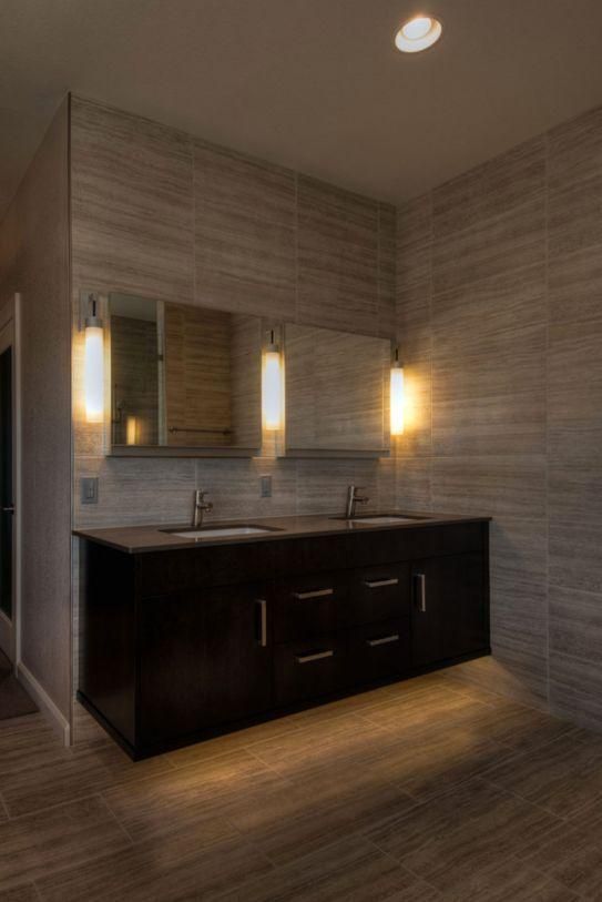 Modern bathroom vanity with dark cabinets, double mirrors, wall sconces, and gray tiled walls and floor