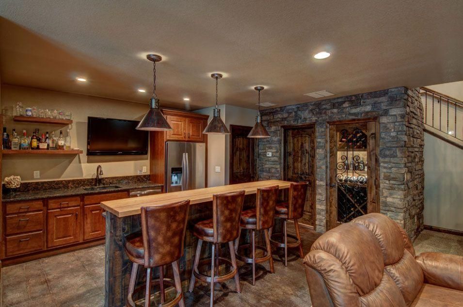 Warm kitchen-bar area with wood cabinetry, stone accents, pendant lights, and leather seating