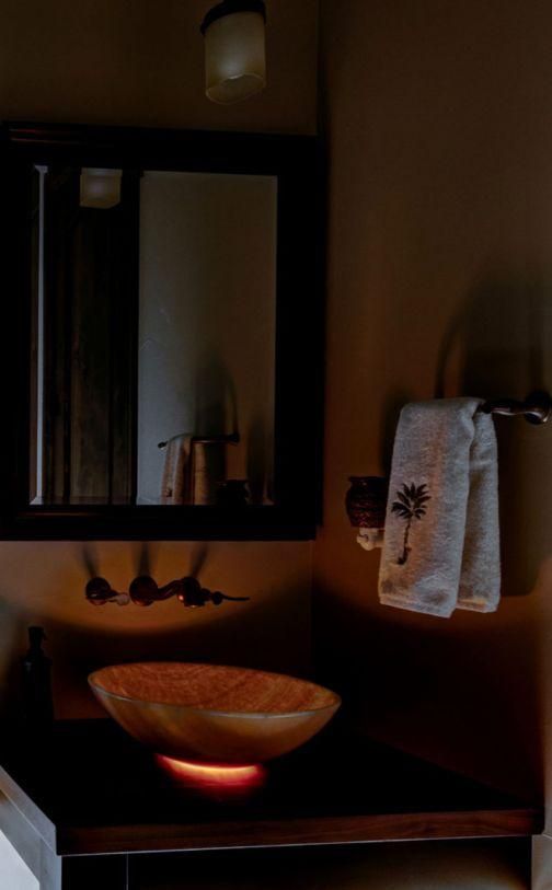 Dim bathroom with a glowing vessel sink, mirror, and towel on the wall.