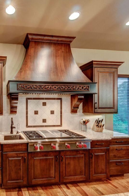 Wooden kitchen with a large range hood, tile backsplash, sink, and recessed ceiling lights.