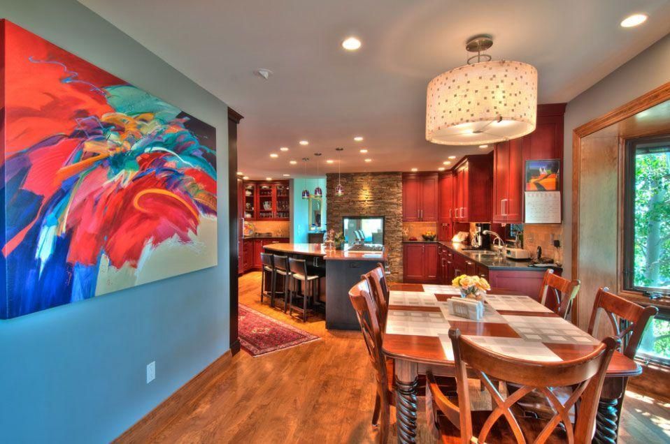 Modern kitchen and dining area with colorful abstract wall art, wood floors, and pendant lighting