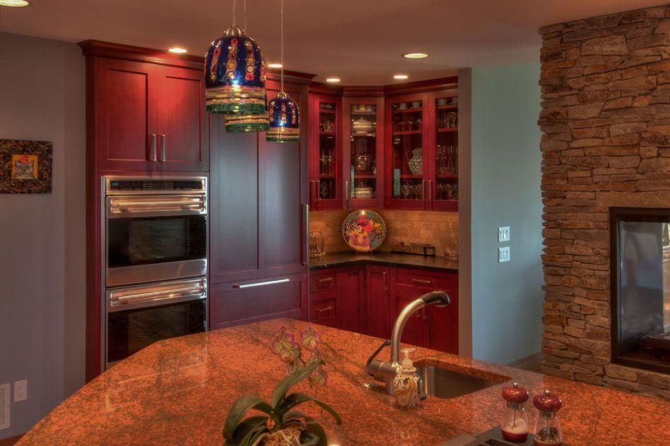 Modern kitchen with cherry cabinets, stone fireplace, stainless appliances, and granite island under pendant lights