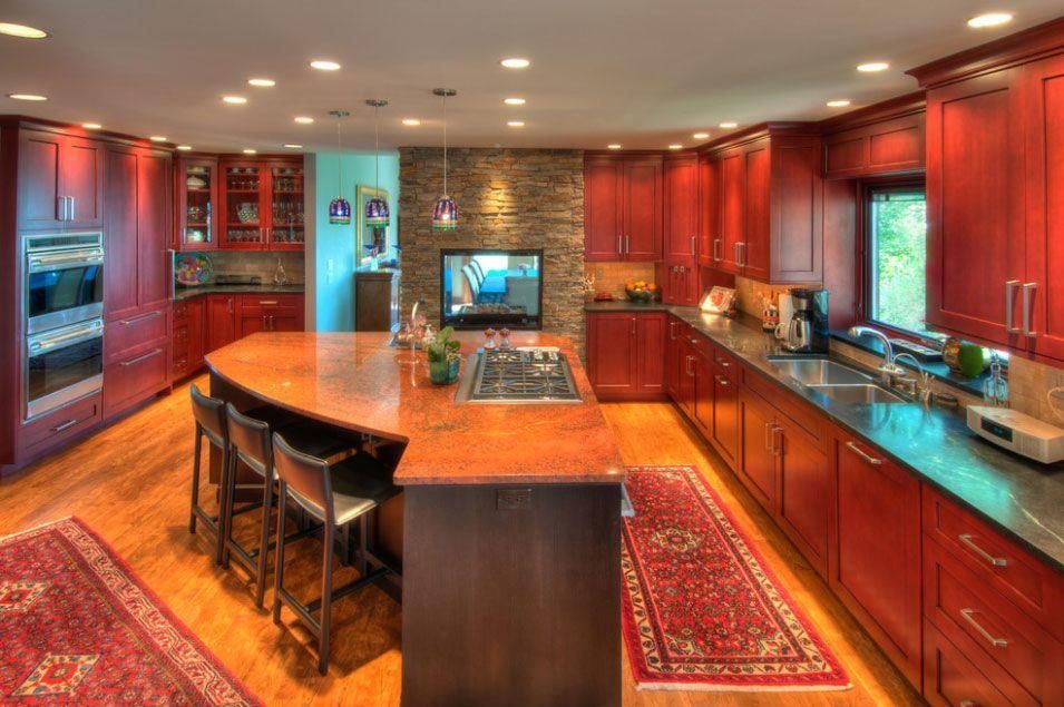 Warm red kitchen with large island, wood cabinets, granite counters, and stainless steel appliances