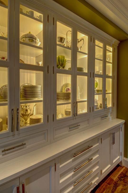 White china cabinet with glass doors, softly lit shelves holding dishes and decor in a warmly lit room