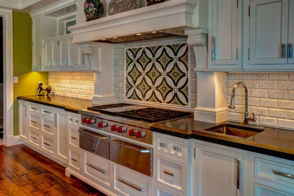 Bright white kitchen with black countertops, red stove knobs, and patterned backsplash under a range hood