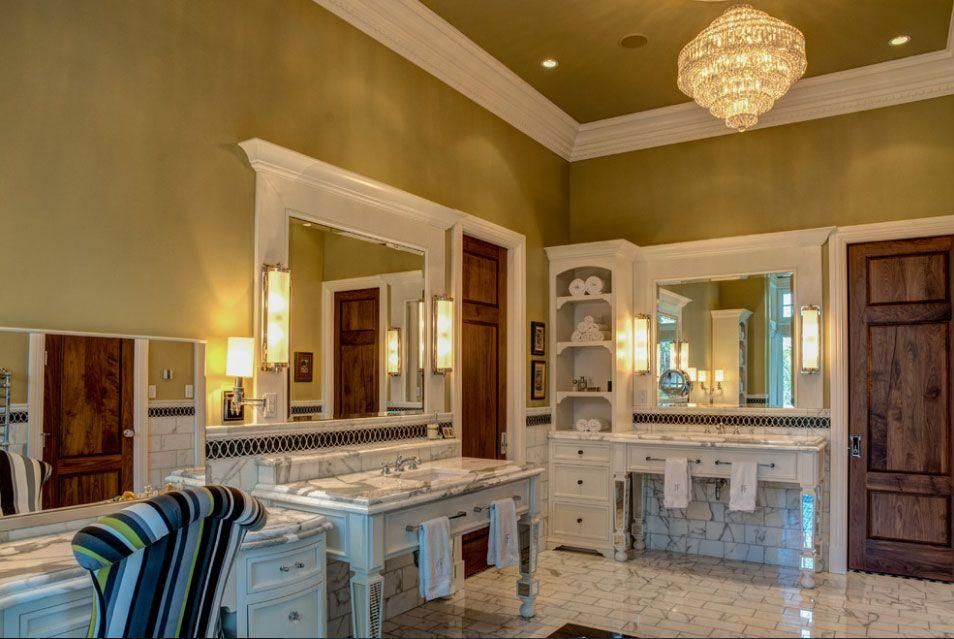 Elegant bathroom with double vanities, large mirrors, and a chandelier under warm lighting