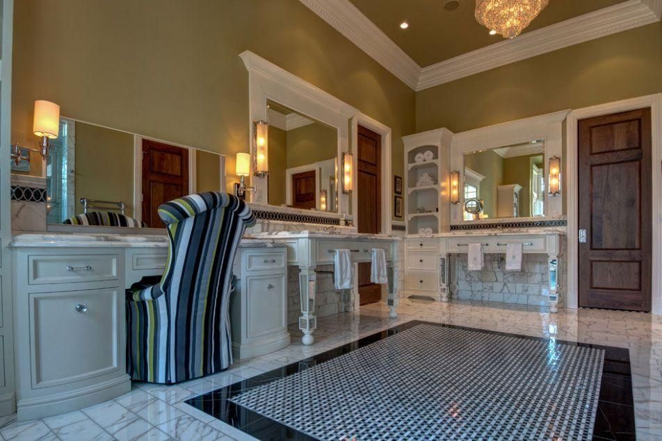 Luxury bathroom with marble vanity, striped chair, large mirror, and dark wood door
