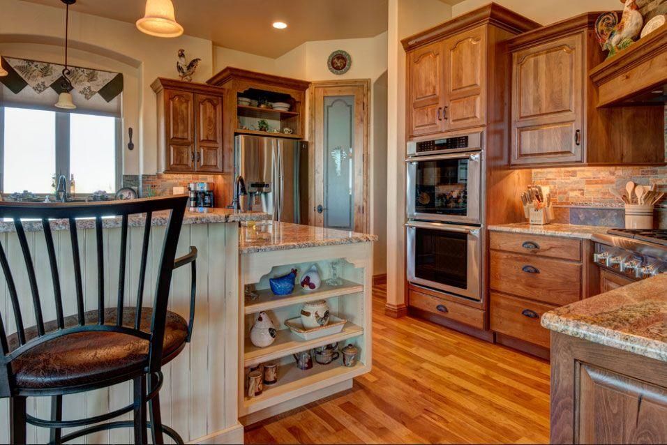Warm kitchen with wood cabinets, granite counters, island cart, and hardwood floors.