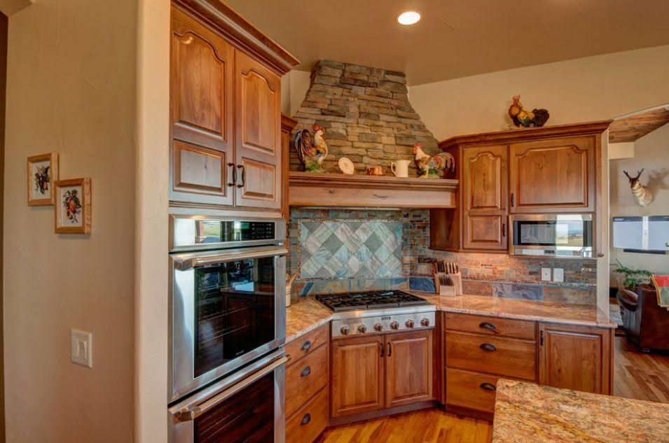 Warm wood kitchen with stone backsplash, stainless oven, and granite countertops