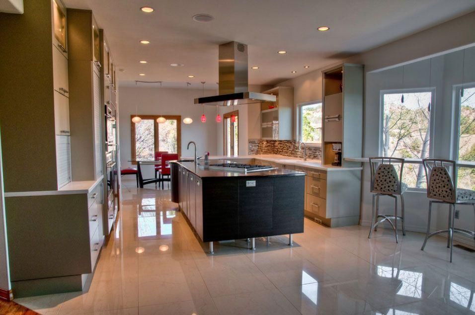 Modern kitchen with glossy island, pendant lights, bar stools, and large windows with outdoor view