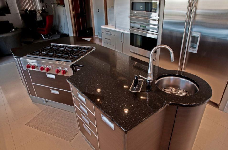 Modern kitchen with stainless steel appliances, dark island countertop, and round sink with tall faucet
