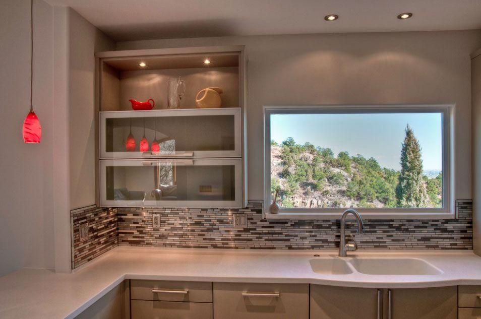 Modern kitchen with open shelves, mosaic backsplash, red pendant lights, and large window overlooking greenery