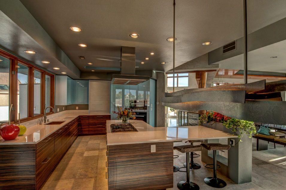 Modern kitchen interior with wood cabinetry, island seating, and large windows overlooking greenery