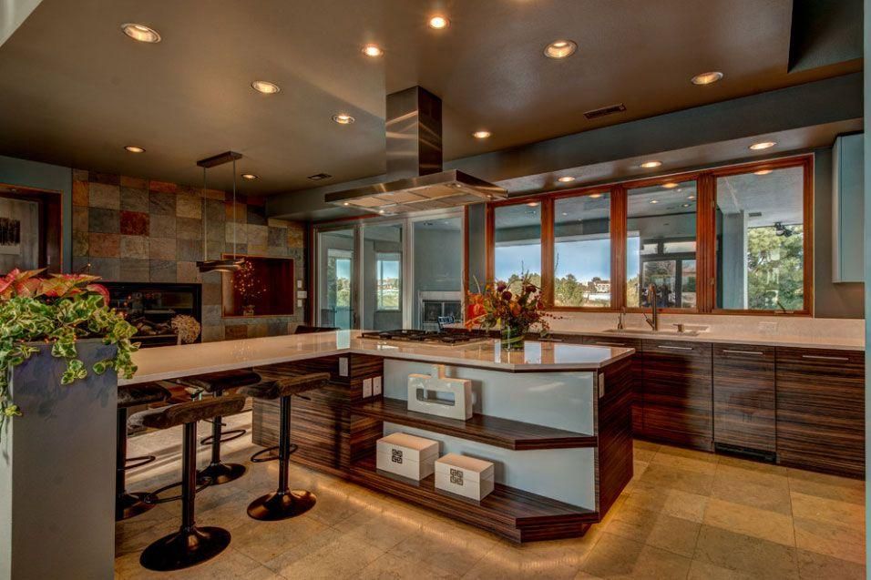 Modern kitchen with large island, dark cabinets, and bright windows overlooking a scenic view