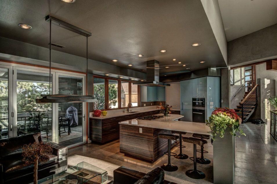 Modern kitchen with dark cabinets, island seating, pendant lights, and large windows overlooking a patio