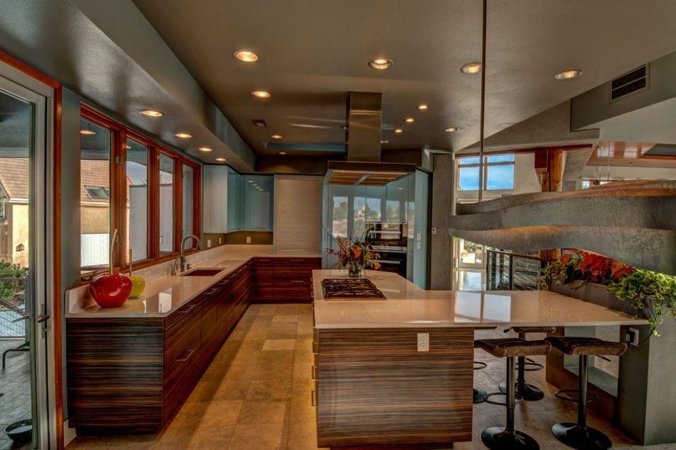 Modern kitchen interior with wood cabinetry, island, bar stools, and large windows