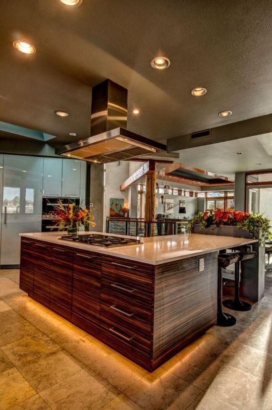 Modern restaurant kitchen island with stainless-steel hood, wood cabinetry, and warm overhead lighting.