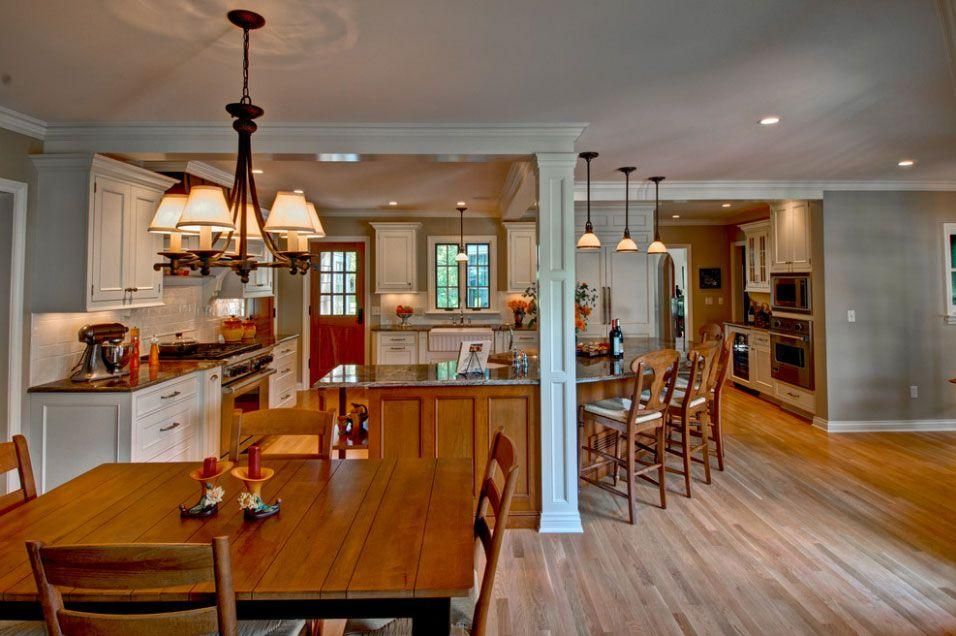 Open-plan kitchen and dining room with wood floors, white columns, and warm pendant lighting