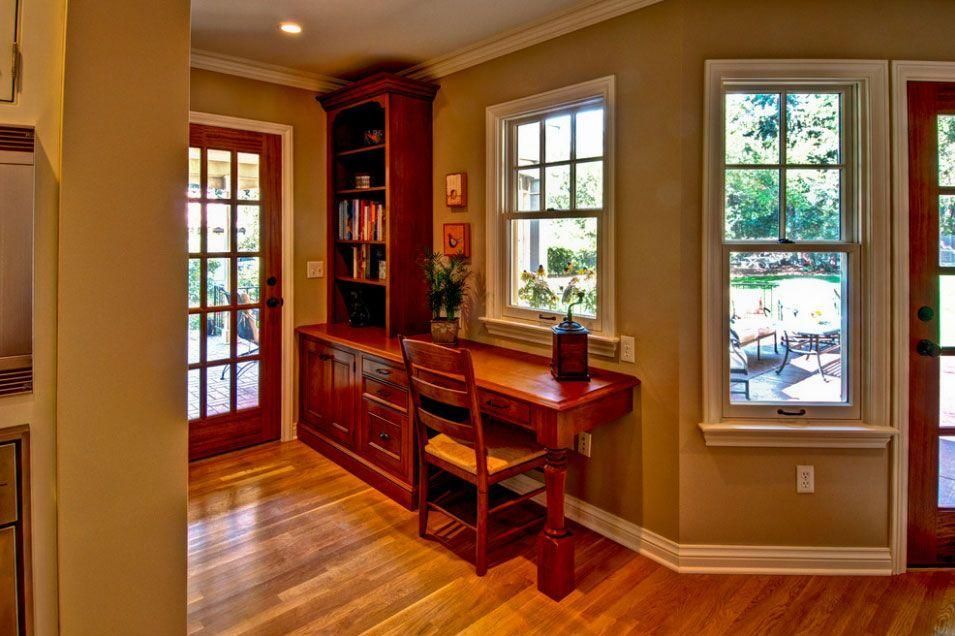 Wood-paneled home office with built-in desk, chair, red door, and sunlight through windows