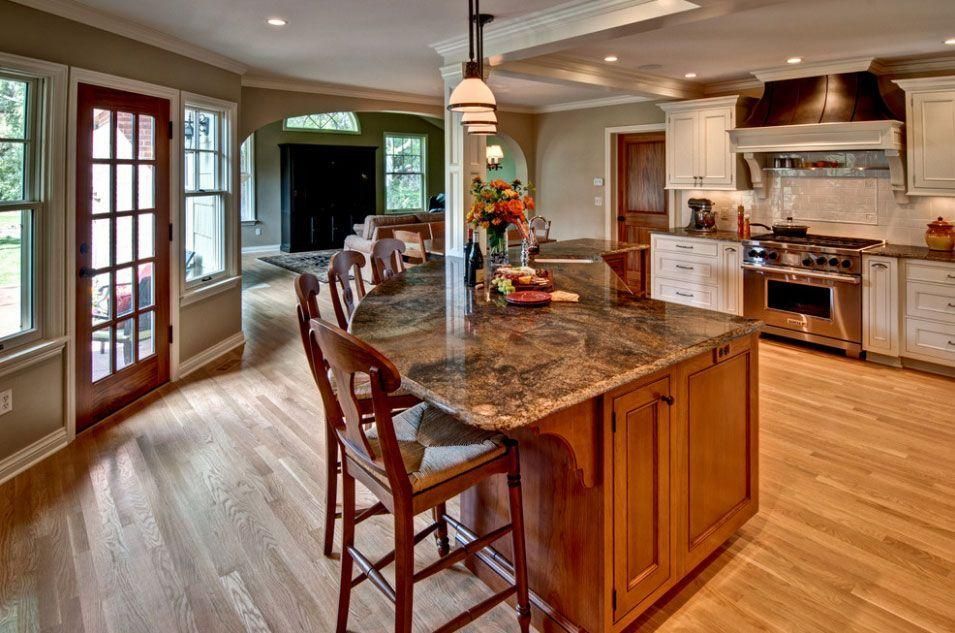 Modern kitchen with granite island, wood floors, and stainless steel appliances, open to a dining area.