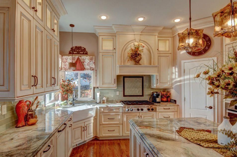 Bright cream-colored kitchen with white cabinets, marble counters, and copper pendant lights