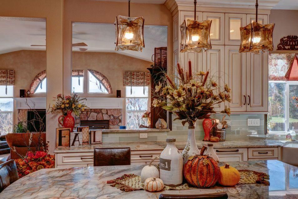 Bright kitchen with fall decor, pumpkins, flowers, and warm pendant lights over a marble island