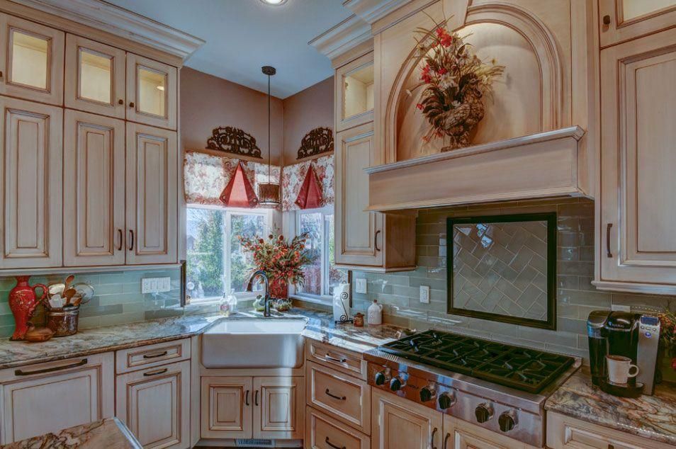 Bright kitchen with cream cabinets, marble counters, a sink under a window, and a stovetop beneath a mantel.