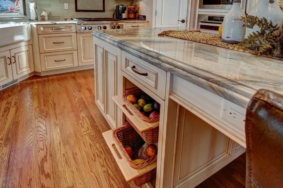 Bright kitchen with white cabinets, marble island, and hardwood floor, featuring a fruit basket and decorative items.