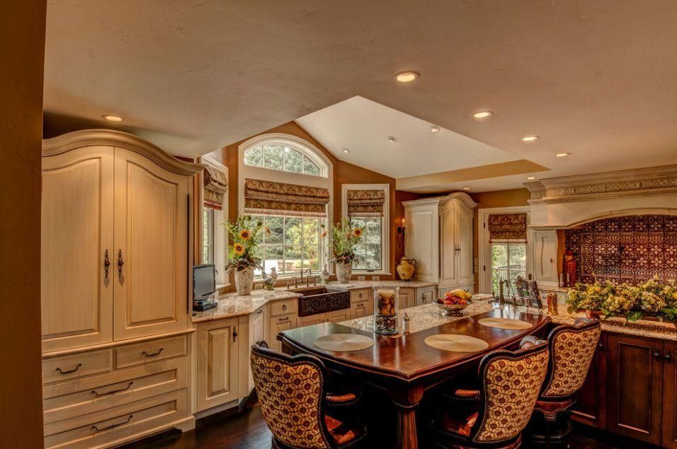 Elegant kitchen with dark wood dining table, beige cabinets, arched window, and warm lighting