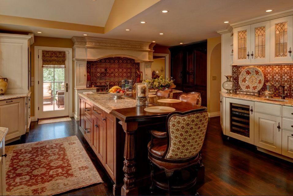 Warm, elegant kitchen with island, patterned chair, ornate cabinets, and dark wood floors