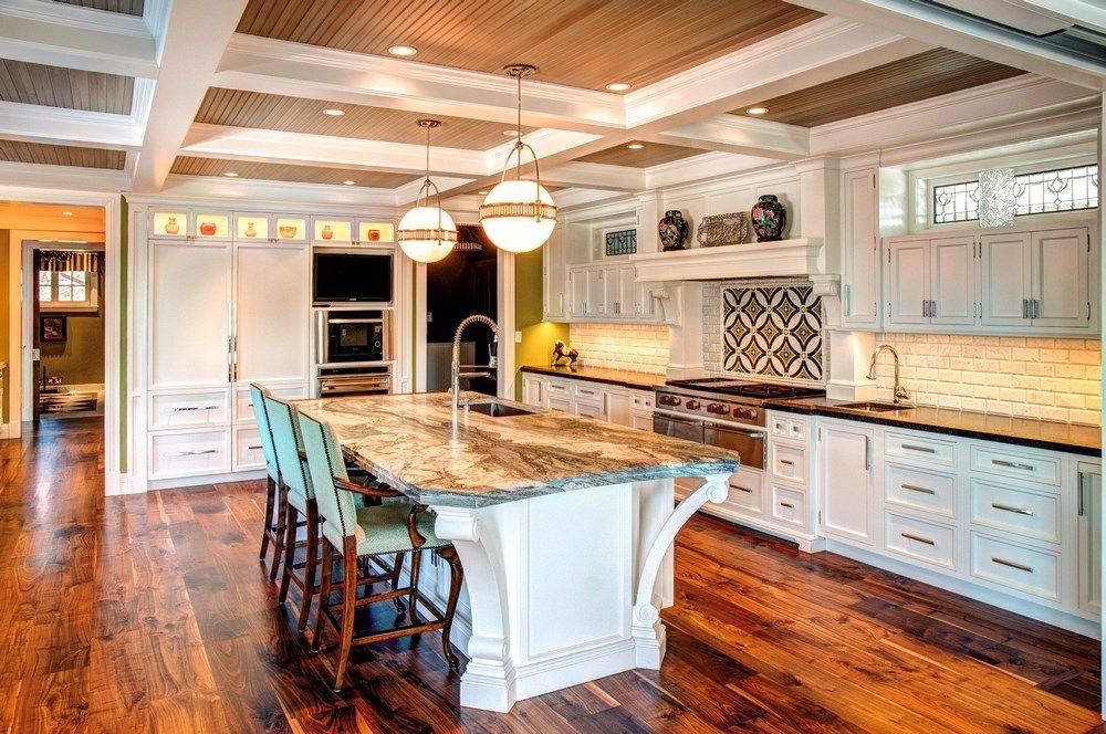 Bright, white kitchen with marble island, dark hardwood floors, and pendant lights