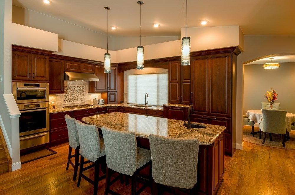 Modern kitchen with dark wood cabinets, granite island, pendant lights, and upholstered barstools