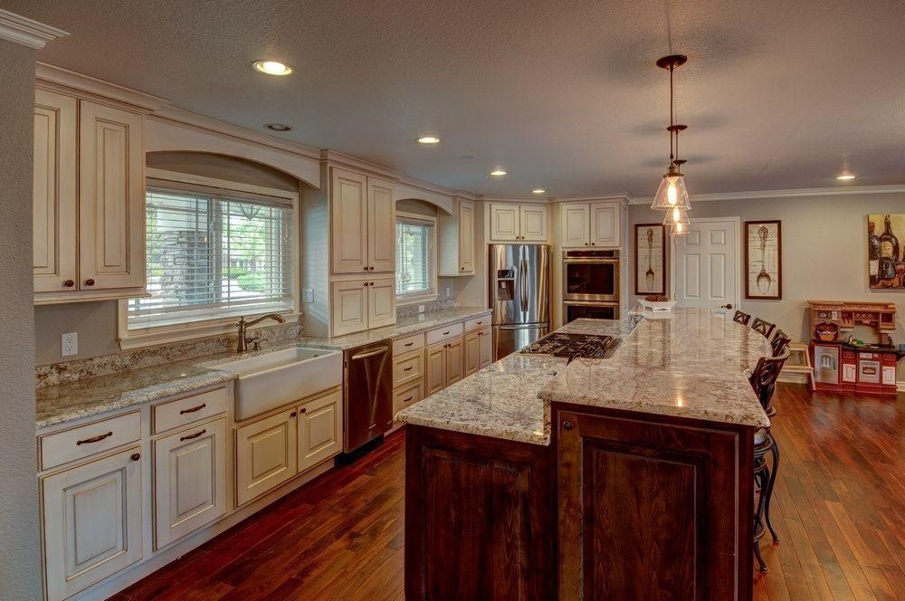 Spacious modern kitchen with white cabinets, granite island, stainless appliances, and hardwood floors.