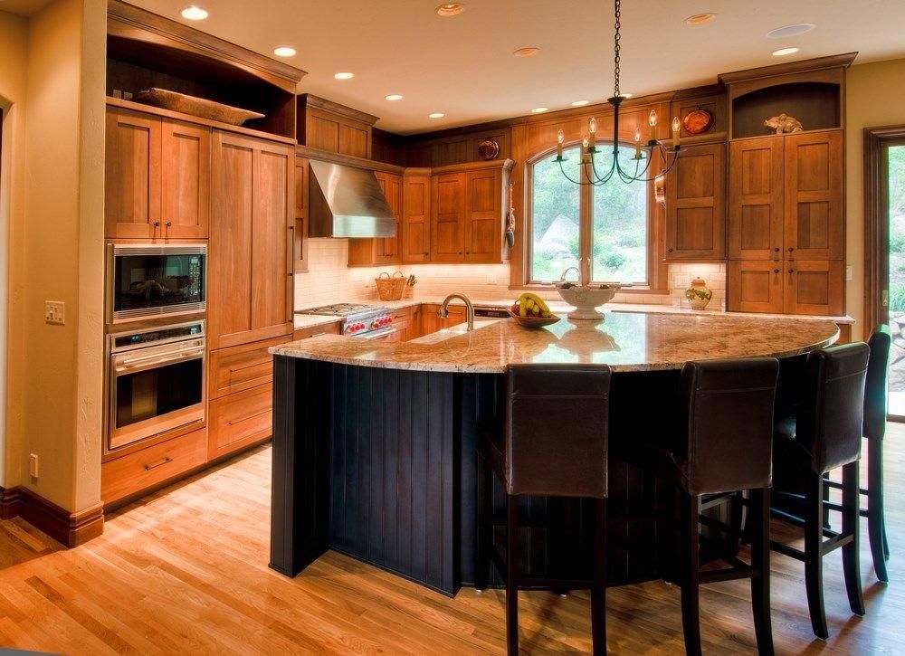 Warm wooden kitchen with granite island, built-in oven, and large window above the sink.
