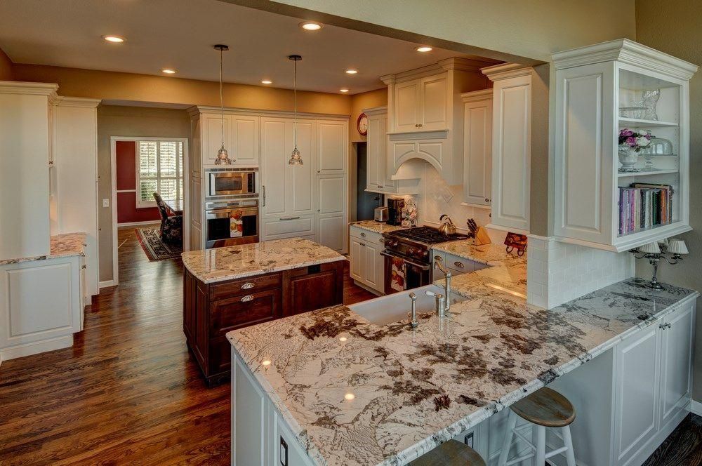 Bright modern kitchen with white cabinets, marble island, wood floors, and stainless steel appliances