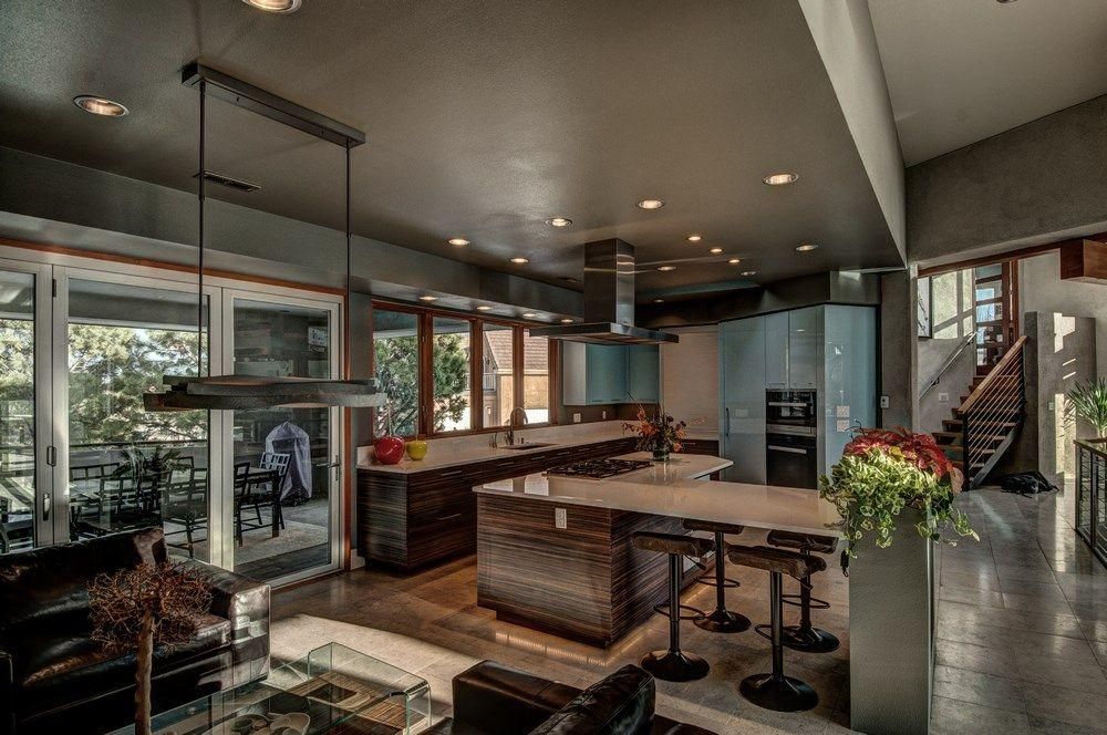 Modern kitchen with island, stools, pendant lights, and large windows overlooking a patio.