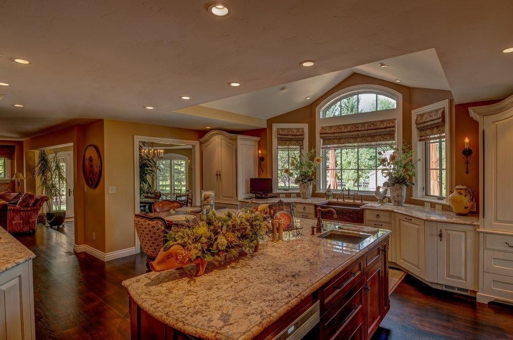 Spacious modern kitchen with granite island, cream cabinets, arched window, and warm recessed lighting